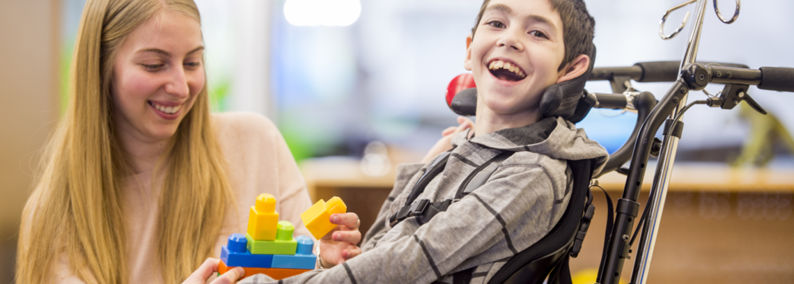 young boy in a wheelchair smiling at the camera while playing with colored blocks
